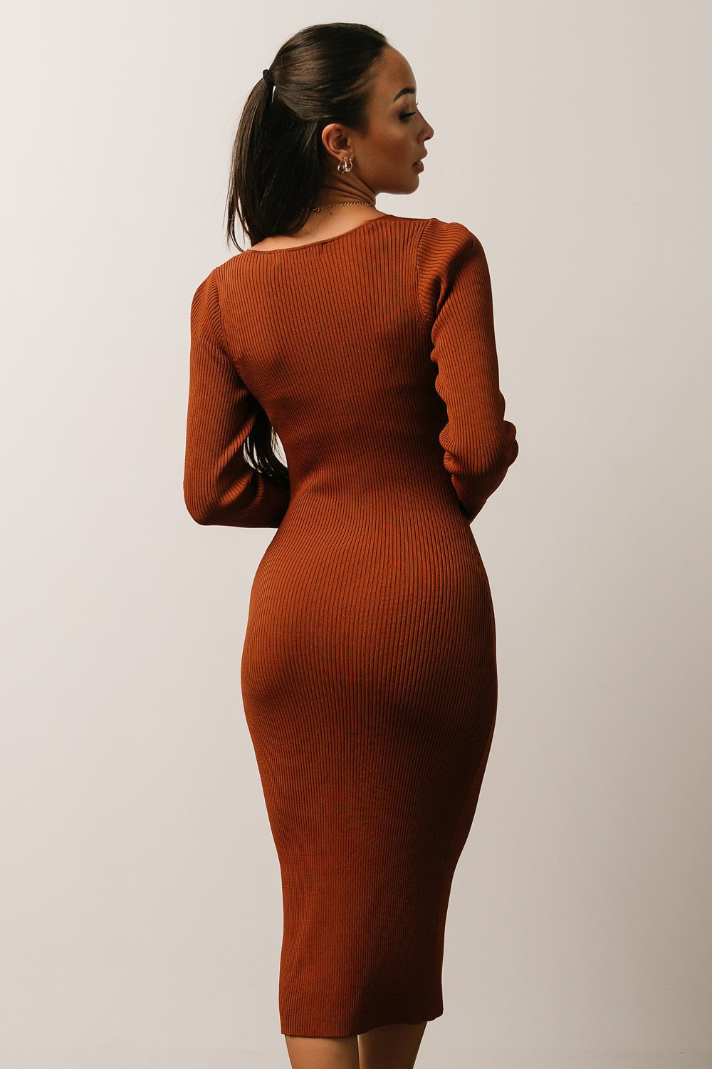 Model seated wearing chestnut ribbed midi dress to show stretch and recovery of the fabric, sweetheart neckline, and fitted silhouette in motion.