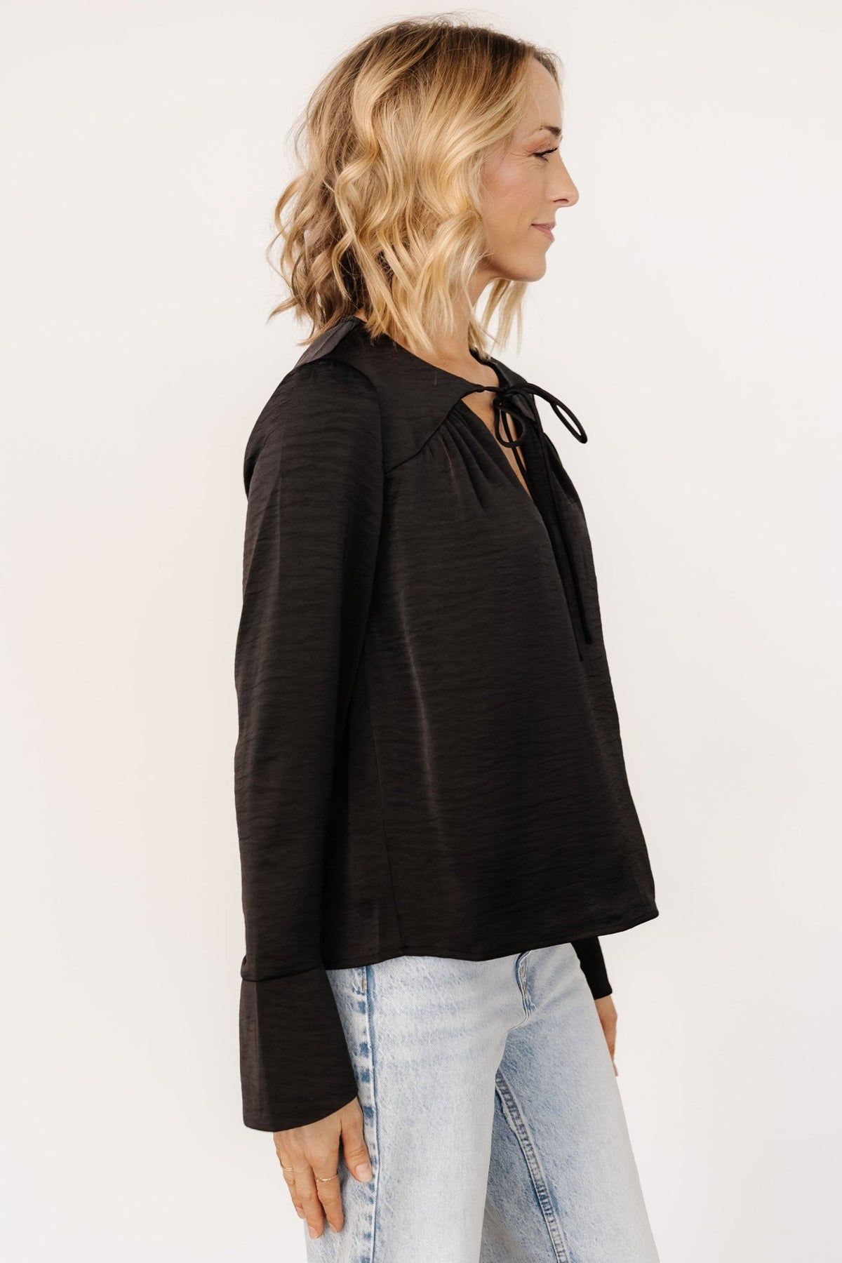 Close-up of the Westminster Satin Top neckline in black showing the V-neck tie, pleat detail, and textured satin-like finish.