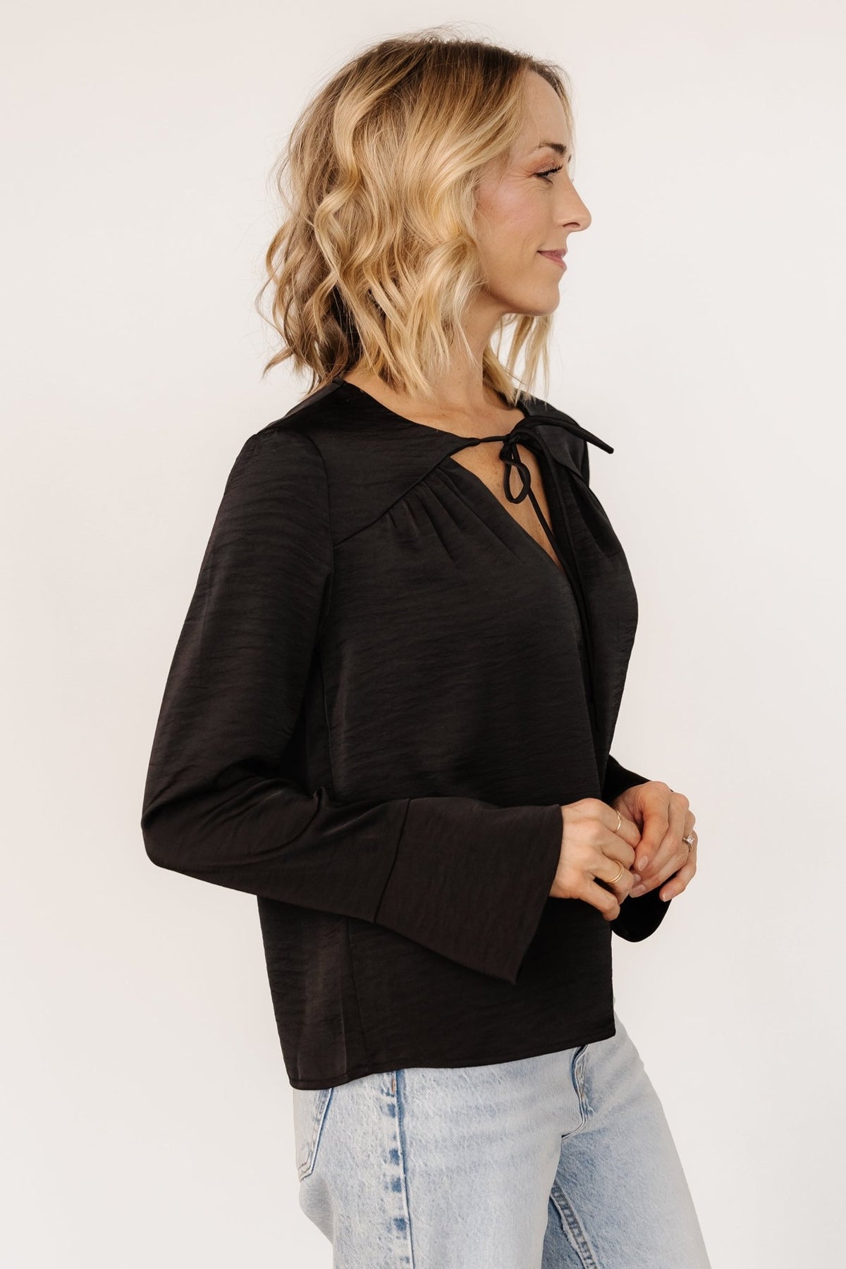 Lifestyle/front view of the Westminster Satin Top in black styled with jeans, illustrating its versatile satin-inspired look for day or night.