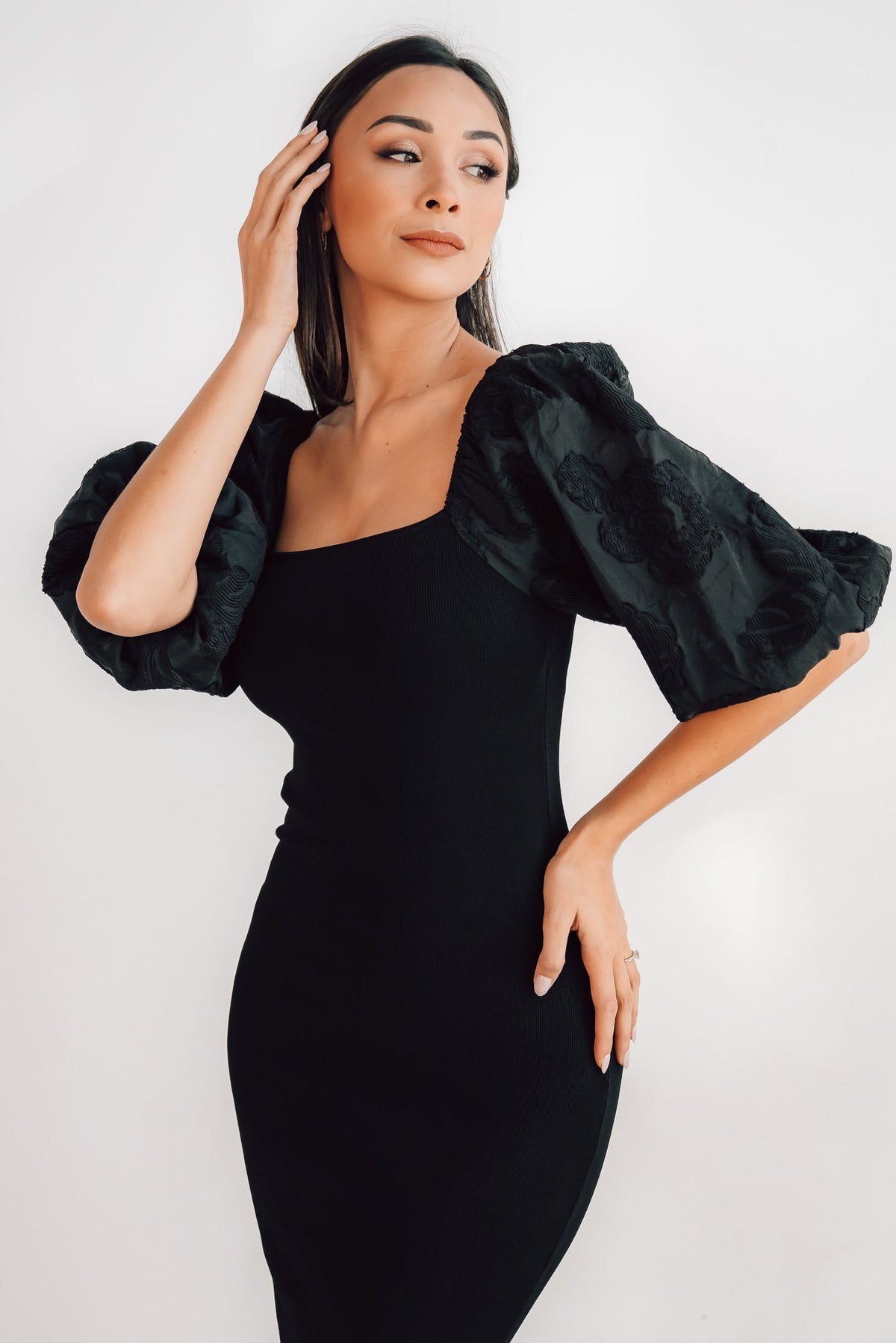 Three-quarter angle of the fitted Weyland black midi dress highlighting the textured embossed sleeve detail and smooth mid-length hem.