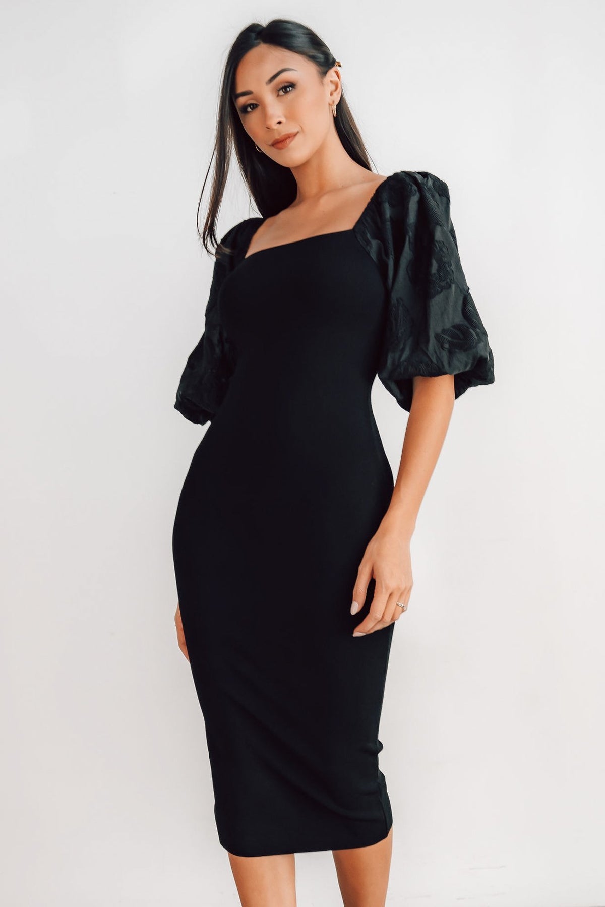 Model wearing the Weyland black midi dress styled with heels; highlights the balanced puff sleeves and tailored bandage-like fit.