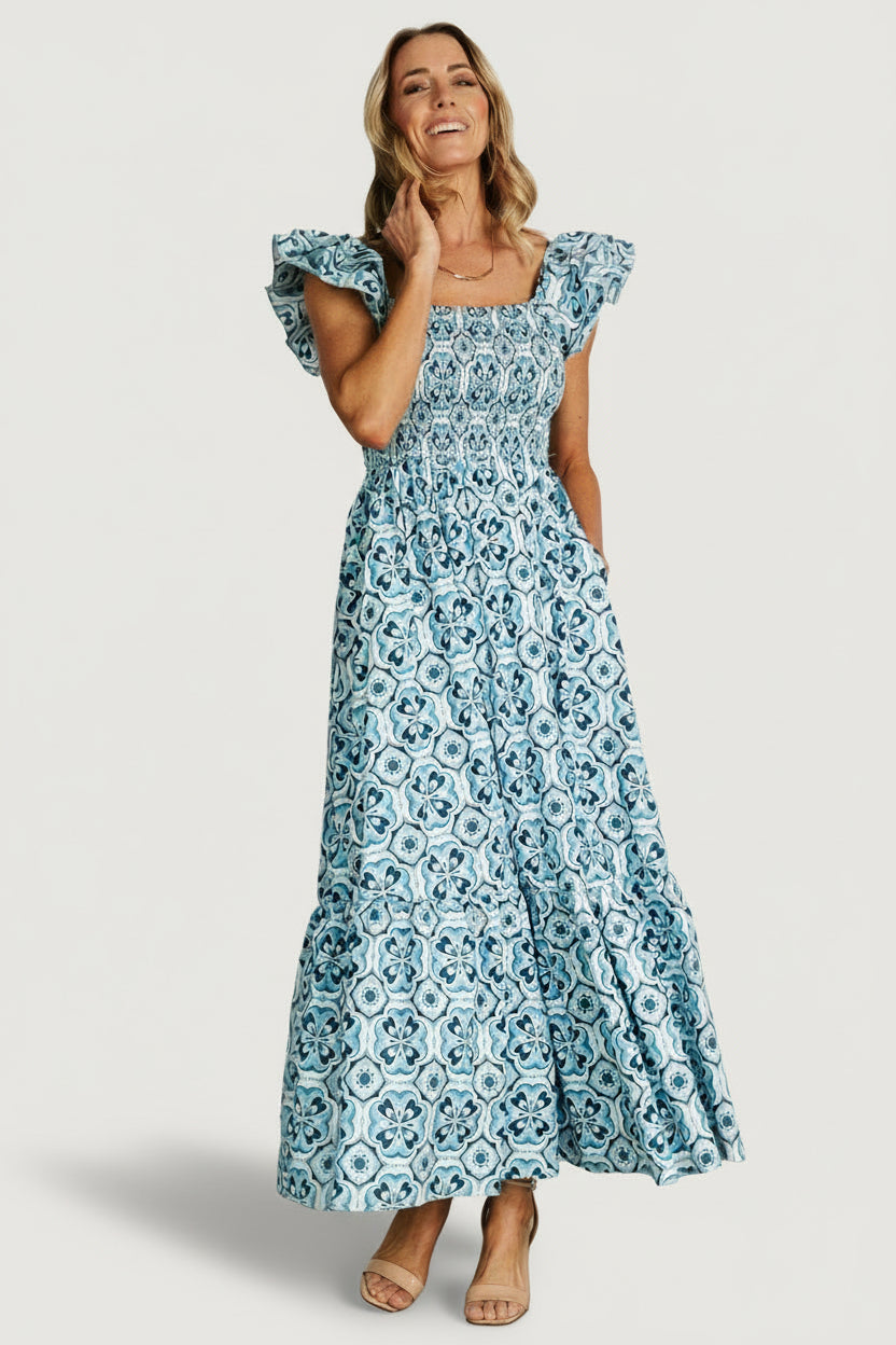 Front view of blue-and-white floral smocked maxi dress showing square neckline, smocked bodice and full single-tiered skirt, pocket visible.