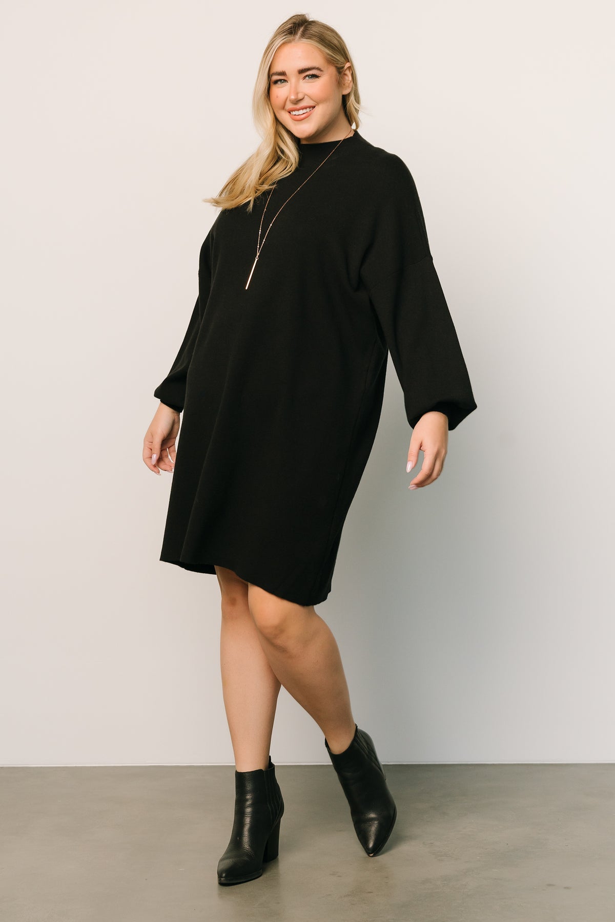 Model wearing the black sweater short dress, hands relaxed at sides, highlighting mock neckline and the gentle drape of the viscose blend fabric.