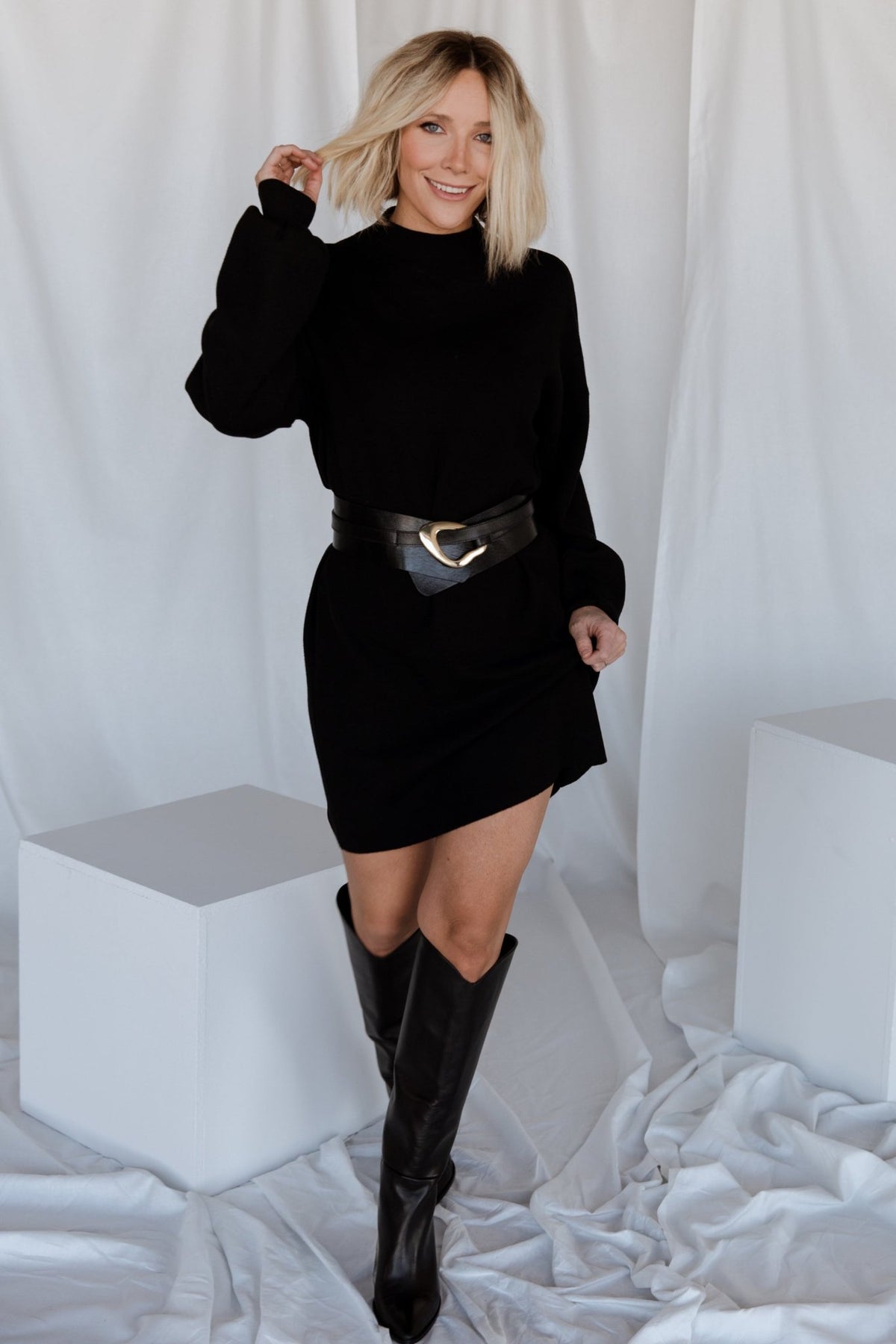 Three-quarter view of black knit sweater dress showing straight silhouette, short hemline, and textured knit across the body for everyday wear.