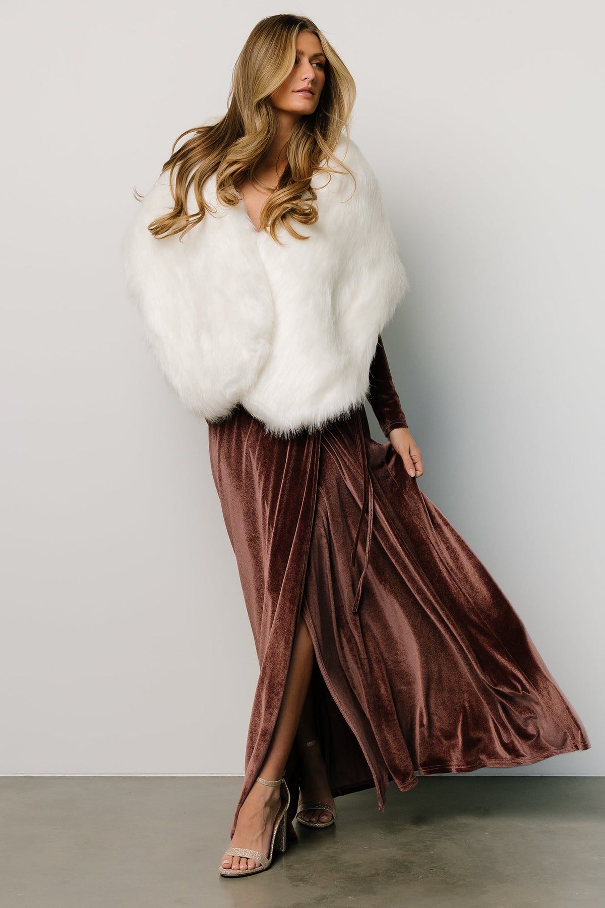 Model wearing off-white faux fur shawl over a gown, front view showing hook-and-eye closure and soft drape across shoulders.