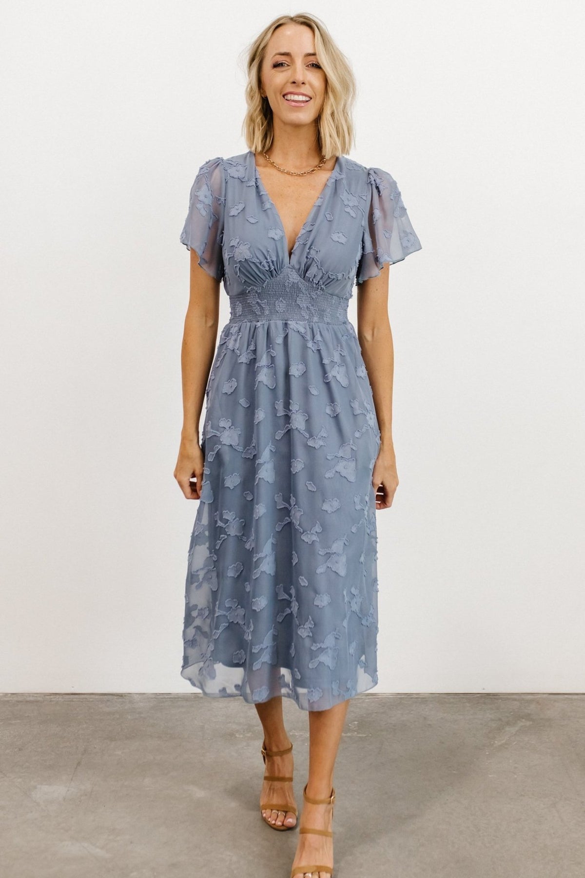Three-quarter angle of blue chiffon midi dress highlighting sleeve silhouette, V-neck pleat detail, and graceful mid-length hemline.