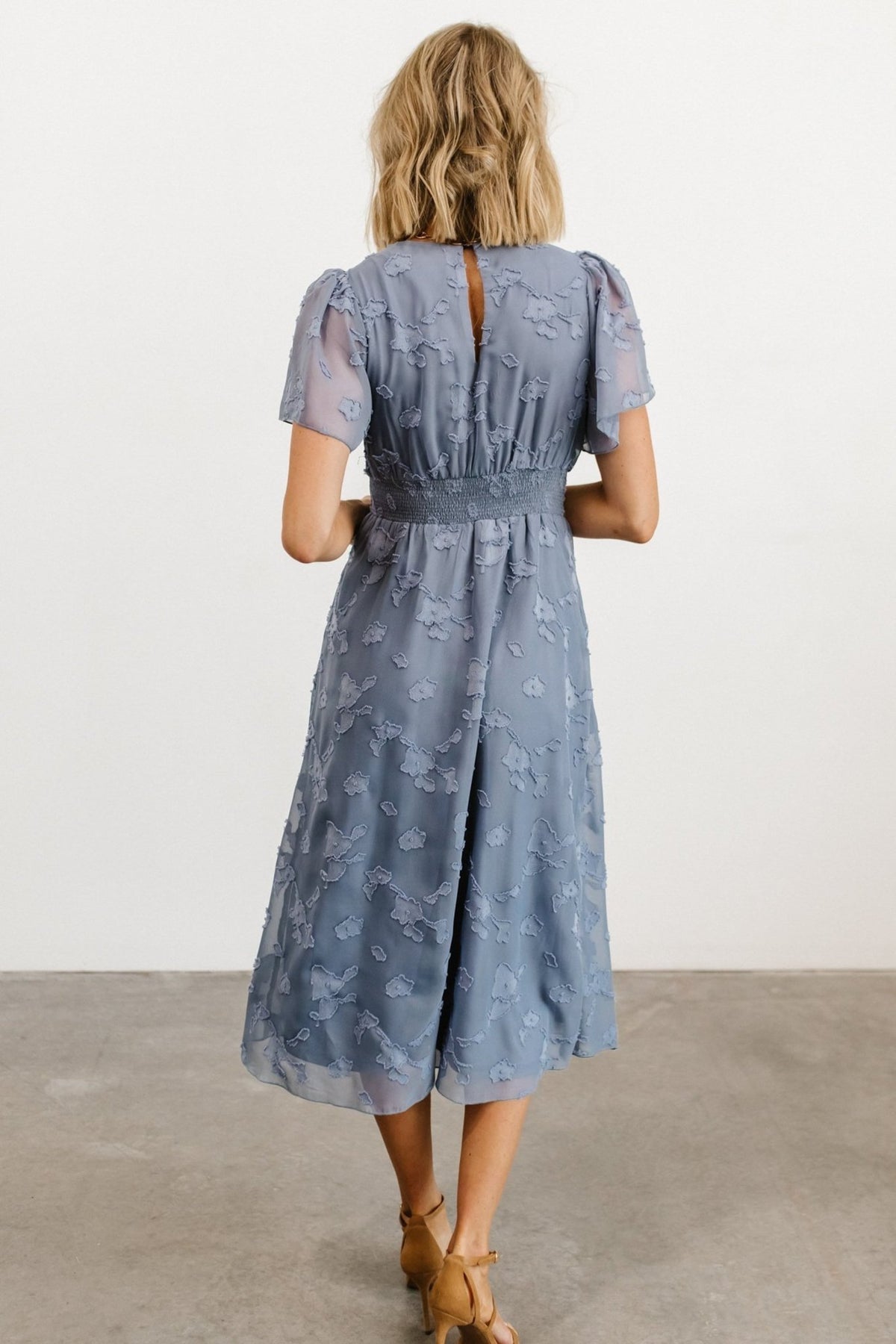 Model wearing blue smocked midi dress styled with neutral shoes, demonstrating the dress’s midi length and flow for daytime events.