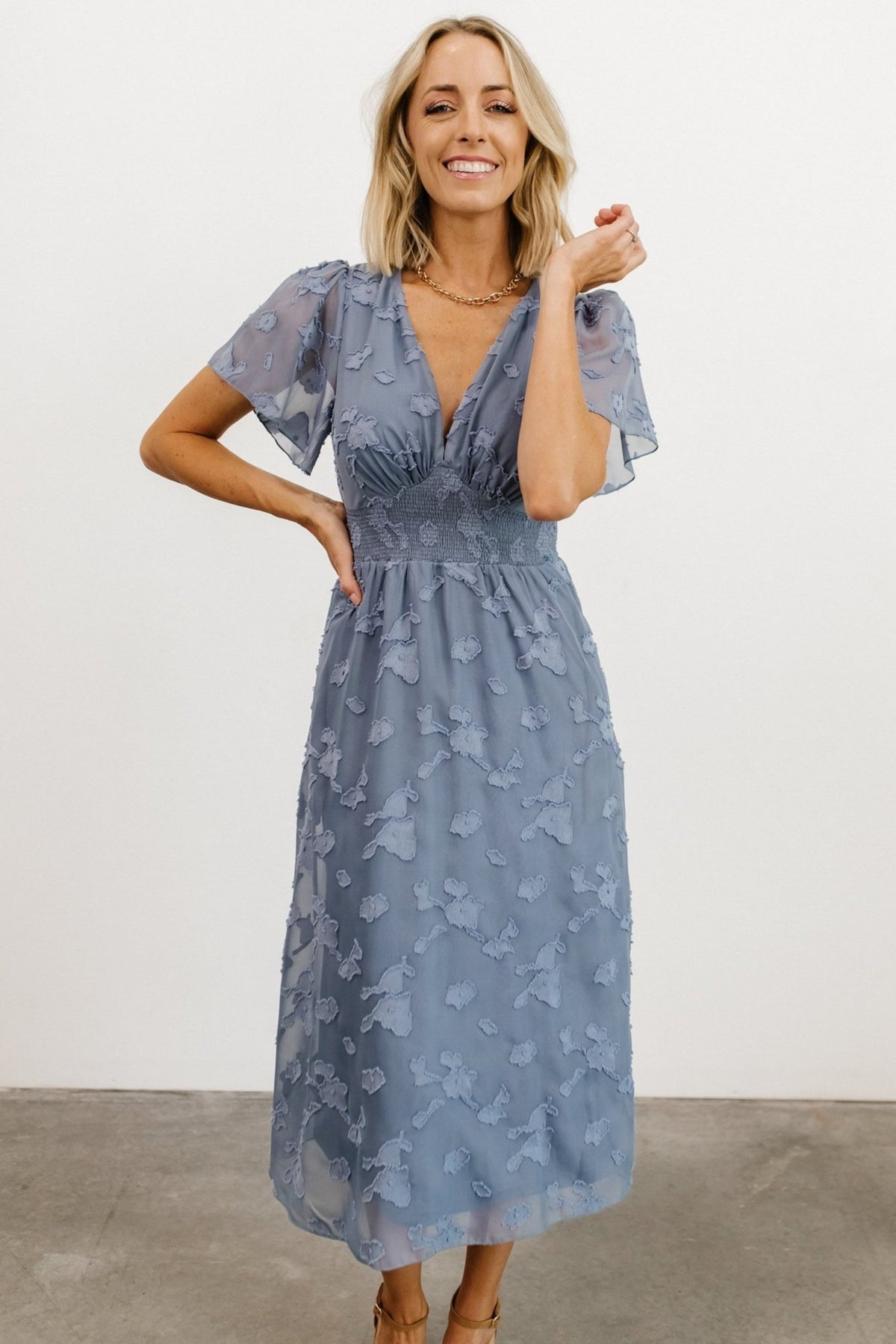 Back view of blue midi dress showing button-and-keyhole closure at the nape and the gathered smocked back for comfortable fit.