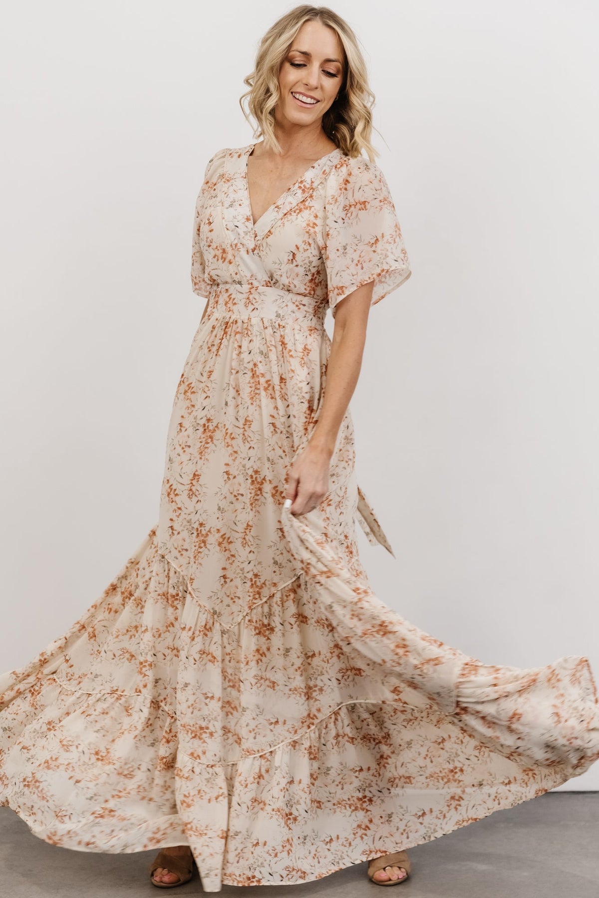 Model wearing cream and rust floral maxi dress, side view highlighting waist ties and flowing chiffon skirt with gentle tiers.