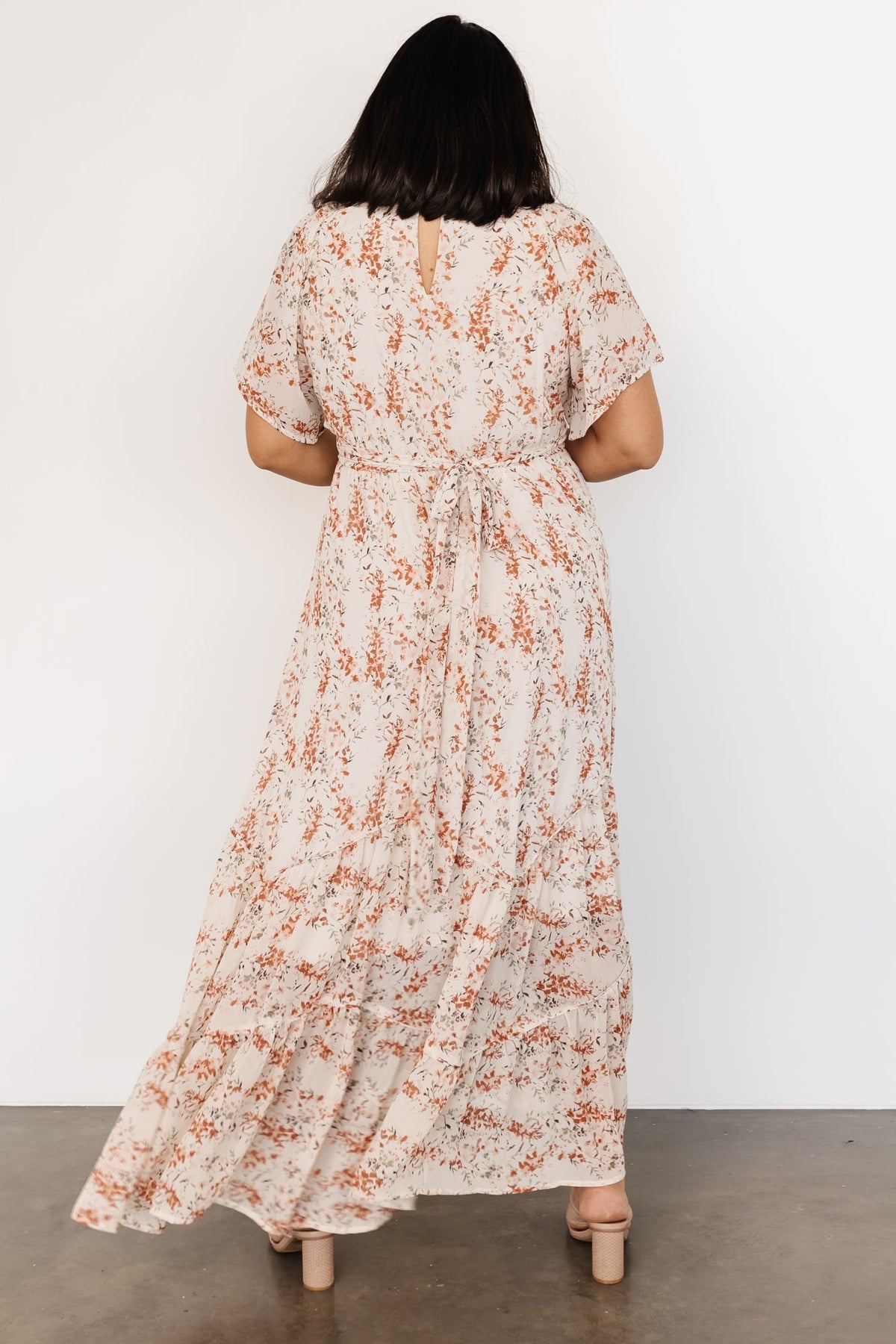 Styled flat-lay of cream and rust floral maxi dress, emphasizing overall silhouette, flutter sleeves, and tiered skirt shape.