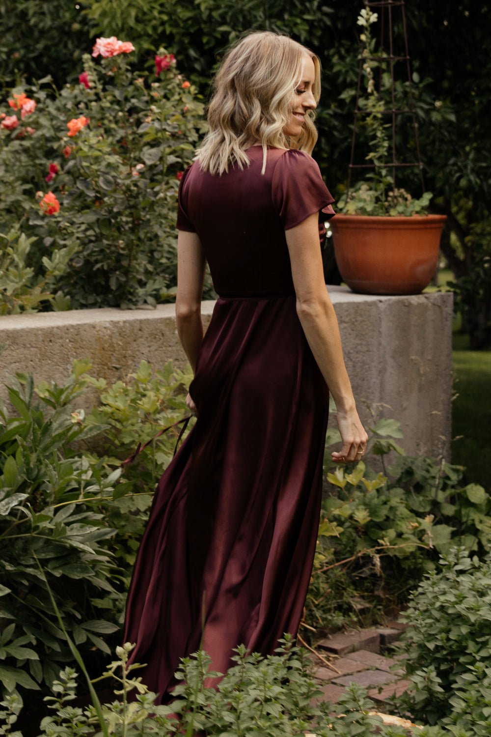 Side view of Krystal Satin Wrap Gown in dark clove displaying tulip skirt overlap and graceful movement of the satin fabric while walking.