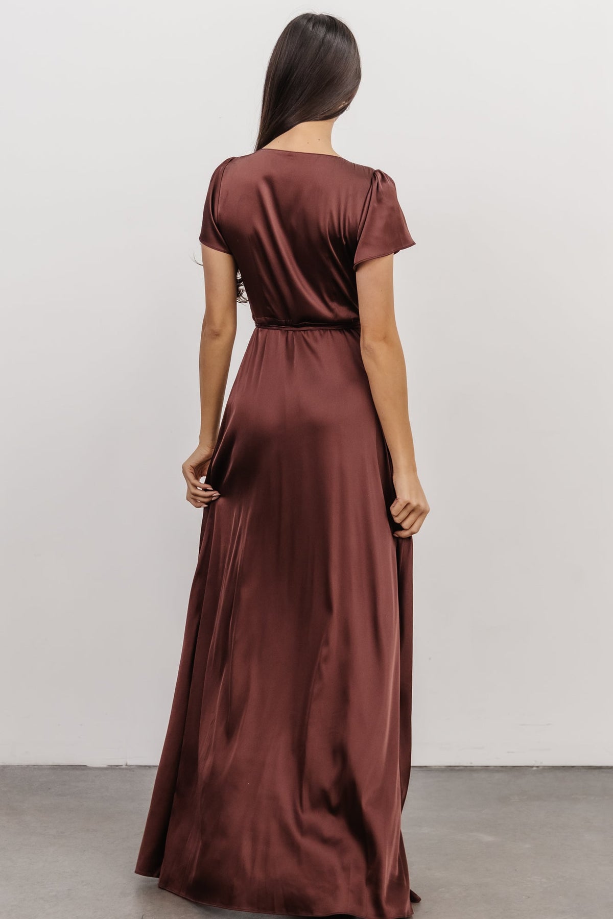 Mid-shot of Krystal Satin Wrap Gown in dark clove highlighting neckline, flutter sleeves and the way the waist ties secure the wrap.