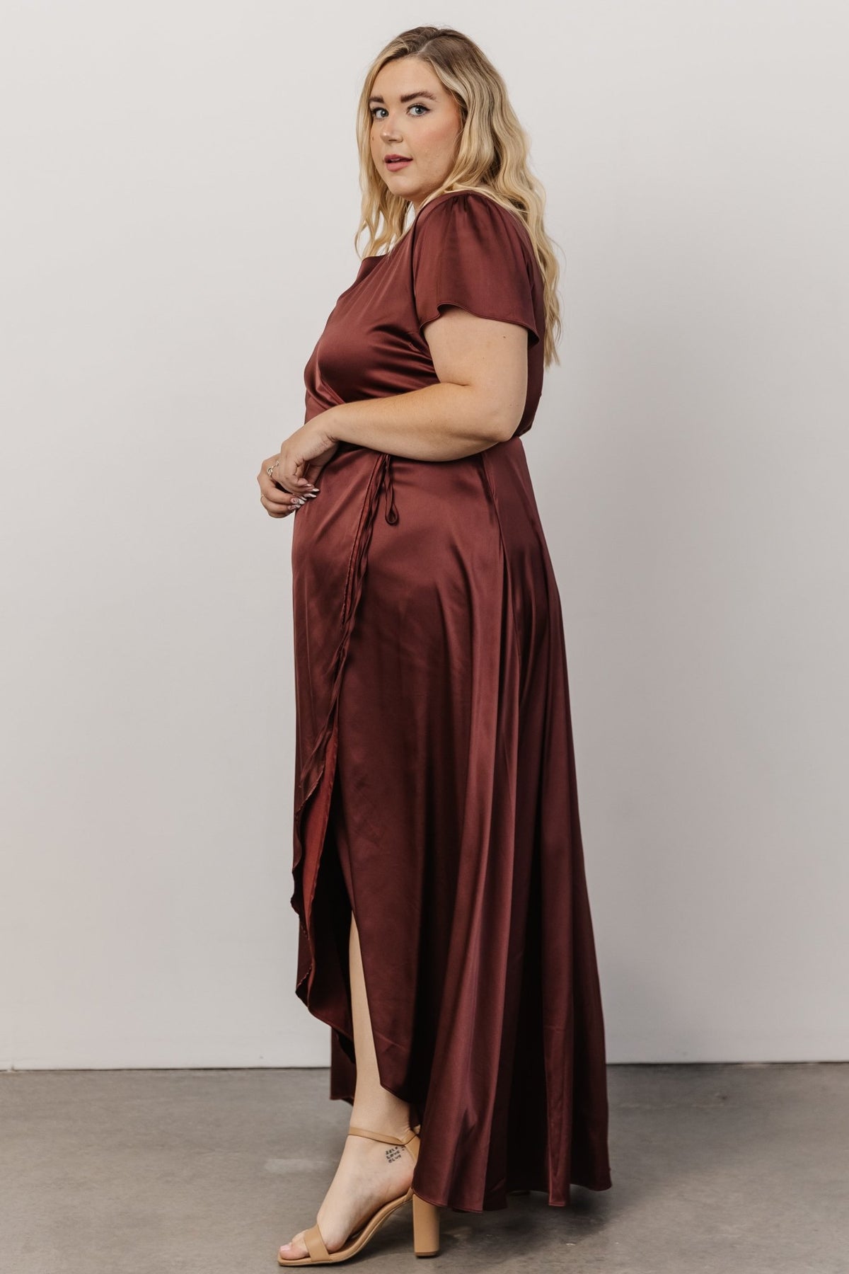 Model walking in Krystal Satin Wrap Gown dark clove, tulip skirt opening slightly to reveal movement and flattering legline.