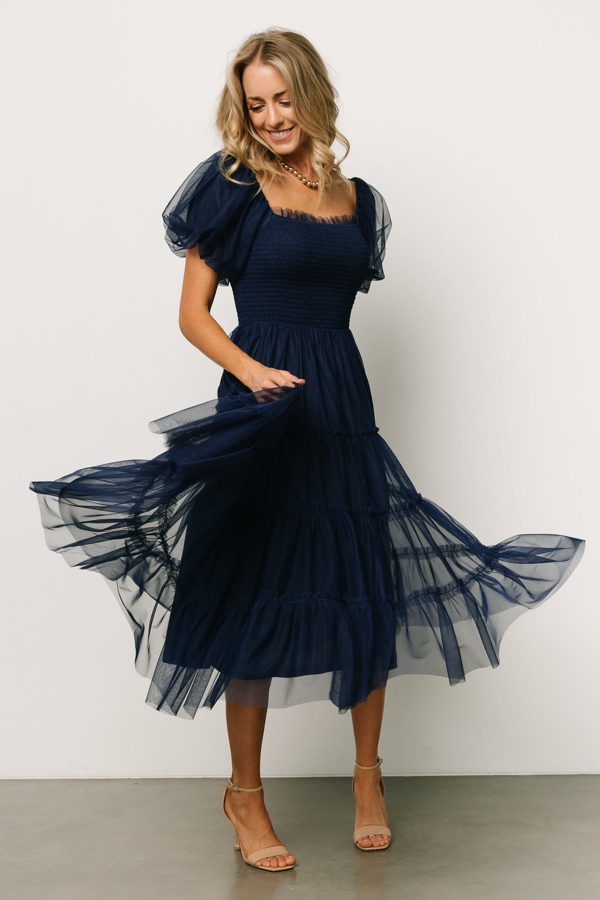 Styled look of the navy Liv tulle midi dress paired with neutral shoes, illustrating length, movement, and occasion-ready styling.