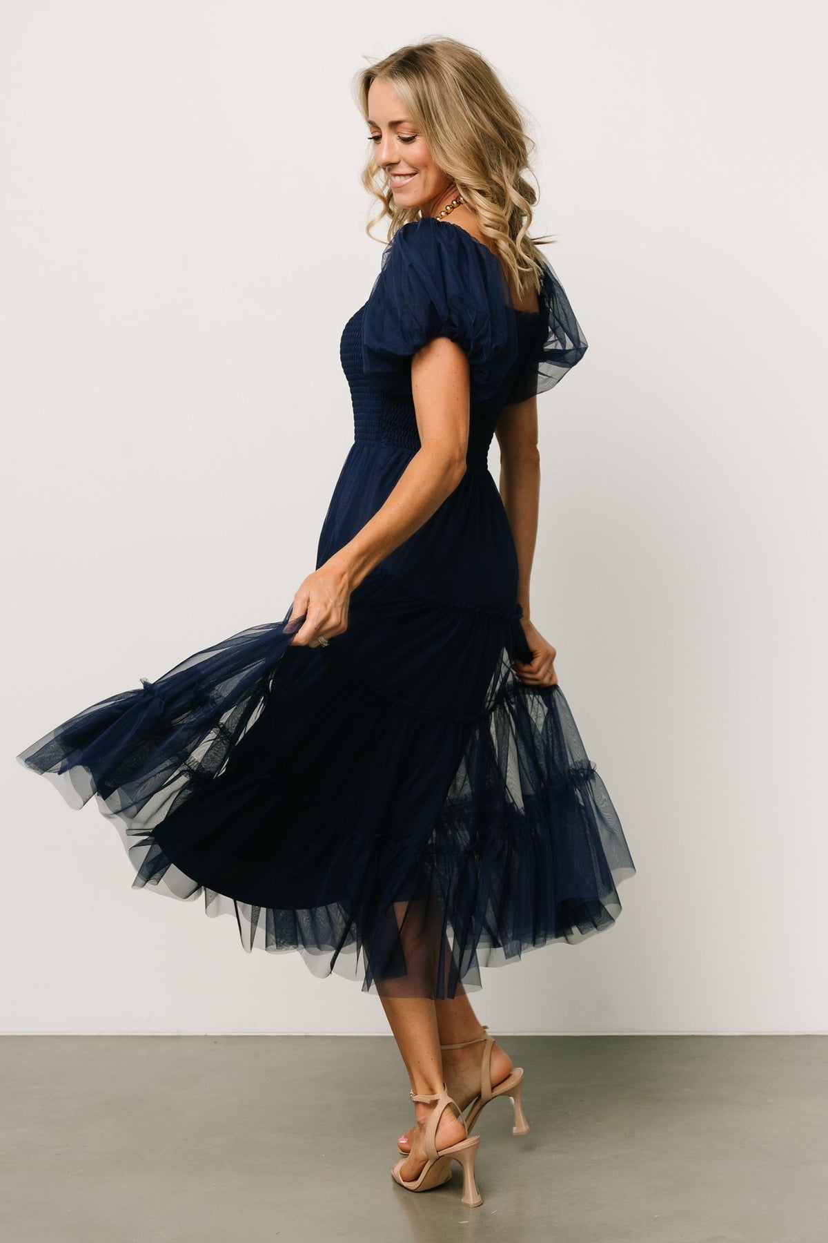 Back and side view of the navy Liv tulle midi dress on model, showing tiered skirt silhouette and overall drape of the tulle.