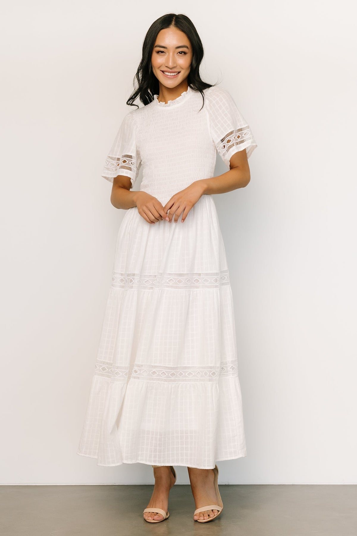 Model wearing off-white Loveland Geo Lace Maxi Dress with hands in side pockets, showing fit and flowing tiered skirt movement.