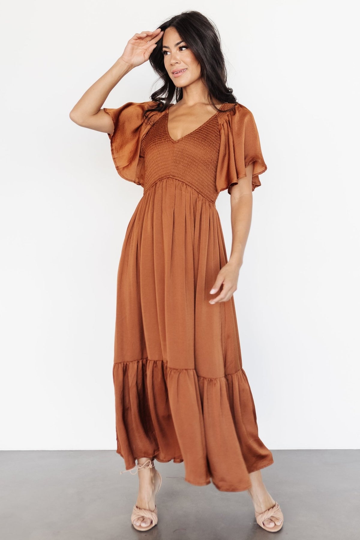 Dark copper satin-like midi dress on model, front view showing smocked elastic bodice, rounded V neckline, and flutter sleeves.