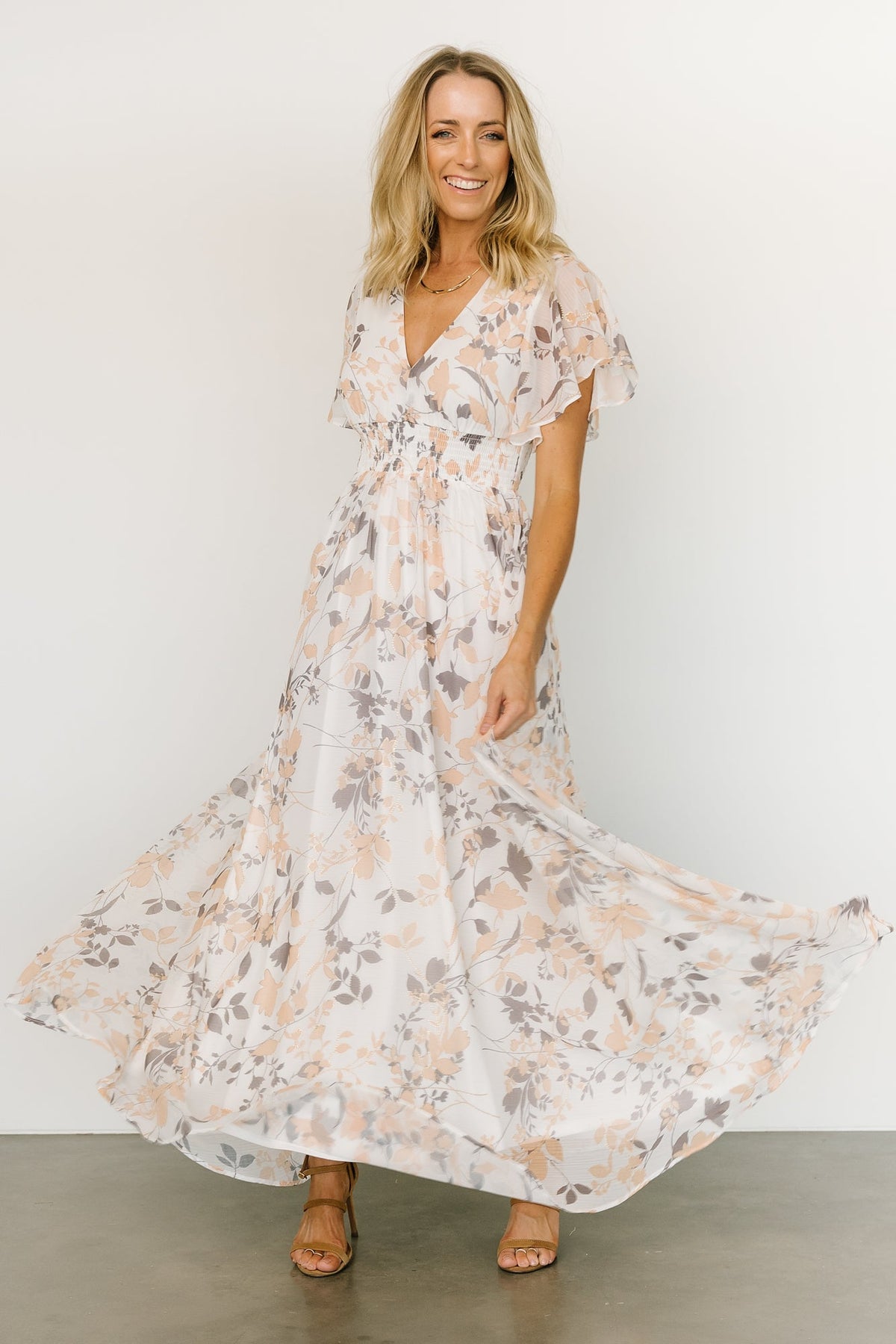 Model wearing off-white printed chiffon Lynlee maxi with subtle metallic thread, flowing A-line skirt and smocked waist; three-quarter front pose.