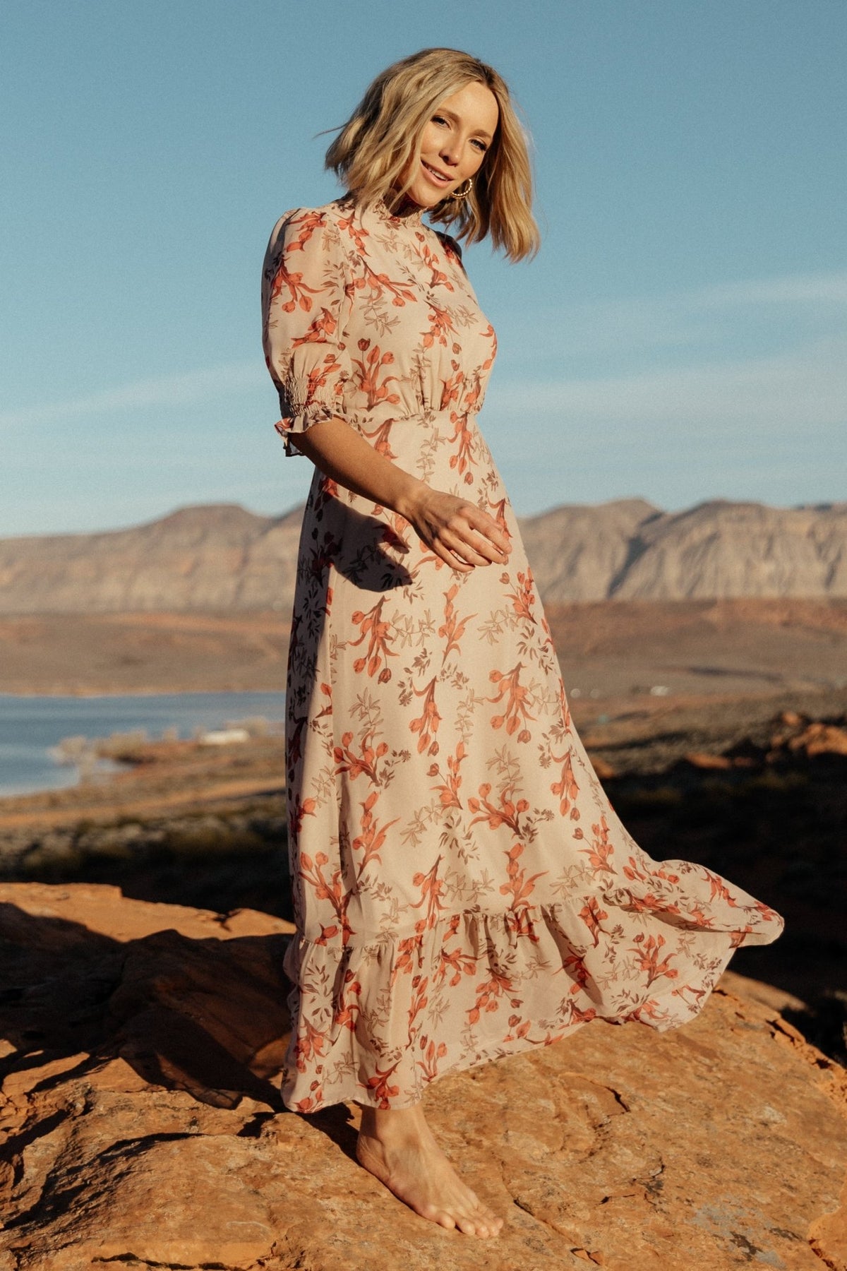 Three-quarter angle of the blush floral chiffon maxi dress highlighting smocked ruffle cuffs and airy sleeve detail with draped skirt movement.