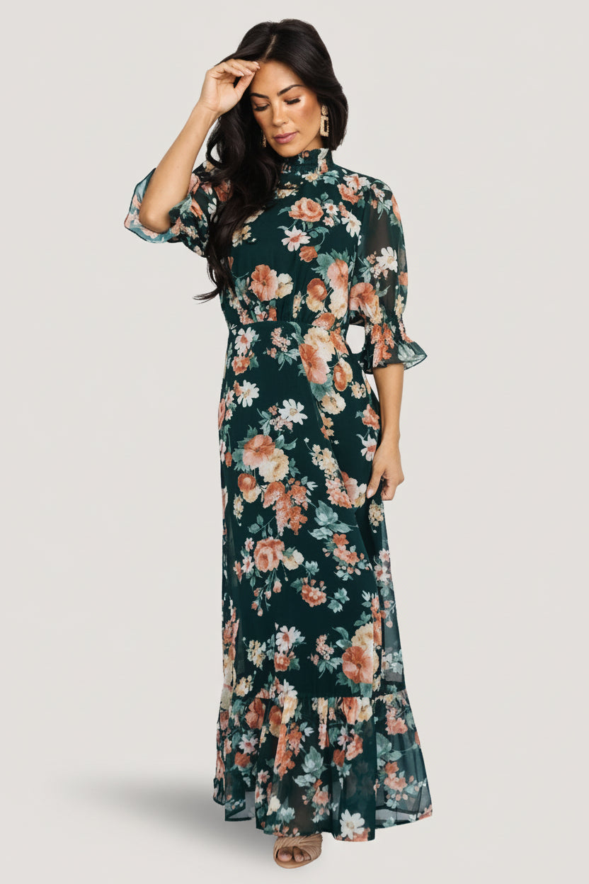 Styled full-length shot of the Marie mock neck maxi dress in dark green floral, paired with heels to show length and drape.