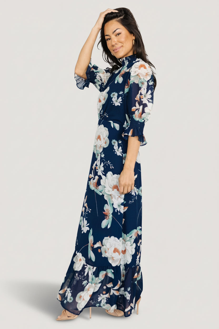 Three-quarter view of the navy floral chiffon dress emphasizing short smocked ruffle cuffs and pleated front waist shaping.