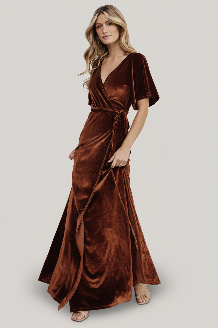 Three-quarter view of bronze velvet wrap dress highlighting mid-length bell sleeve, bodice drape, and the tulip hem movement on a model.