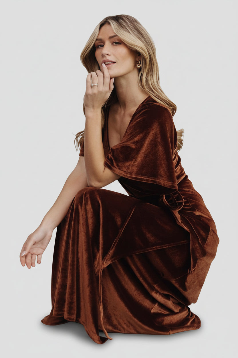 Product flat-lay of Meghan bronze velvet wrap maxi showing V-neck, waist tie, tulip hem and fabric sheen on a neutral background.
