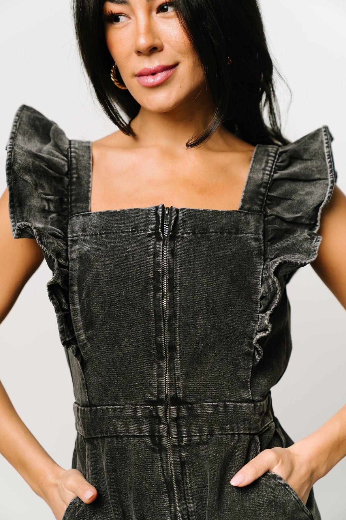 Image showing functional front pockets and the overall short silhouette of the Montgomery washed black denim romper for casual wear.