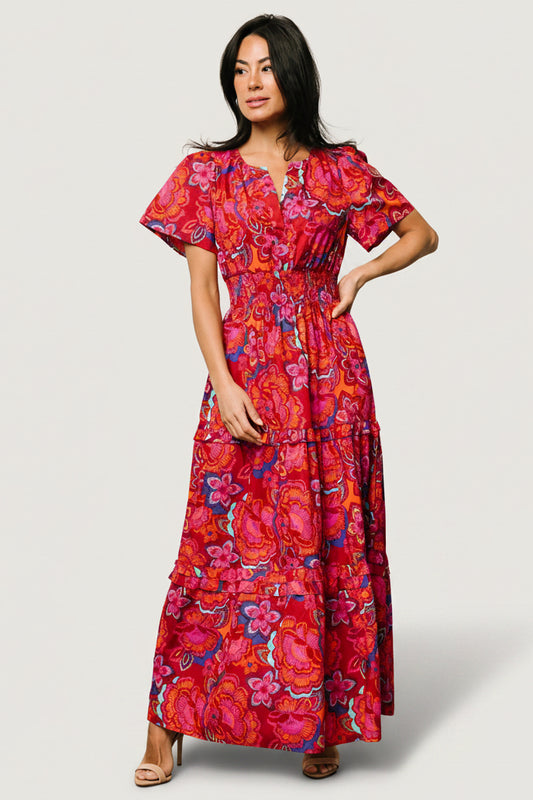Three-quarter view of Palmer Maxi Dress highlighting tiered ruffled skirt, flowing hem, and the dress’s vibrant red, pink, orange, and blue floral pattern.