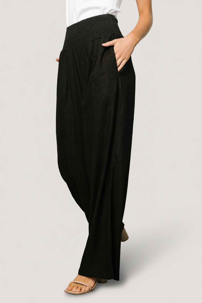 Lifestyle image of Parvati smocked high-waist pants in black, styled with a tucked top to show waist detail.
