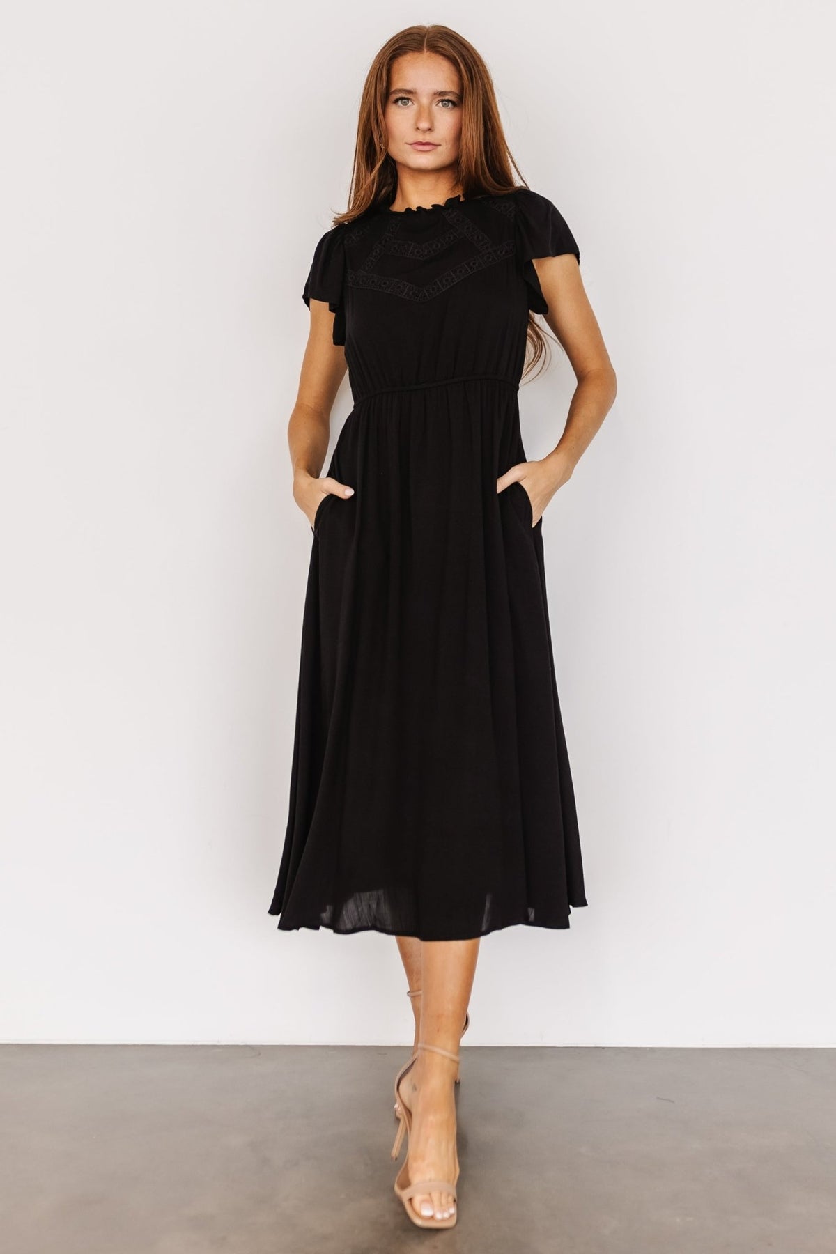 Front view of black Prestyn midi dress showing eyelet lace bodice, ruffle-trim neckline, elastic waist and side pockets for everyday wear.