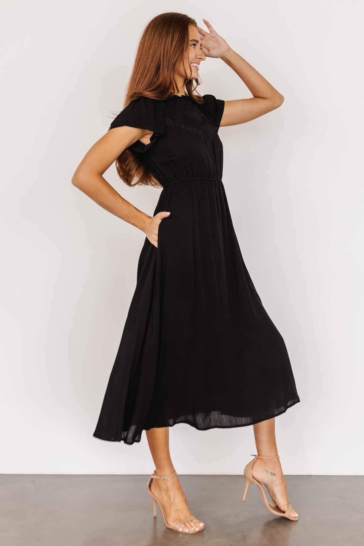 Three-quarter view of the black Prestyn midi dress highlighting the eyelet lace detail, ruffle neckline and the dress silhouette.