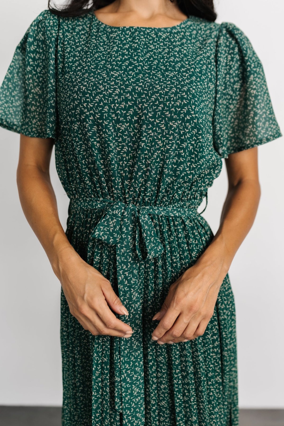Front view of green floral pleated midi dress showing round neckline, short sleeves, and softly pleated skirt detail.