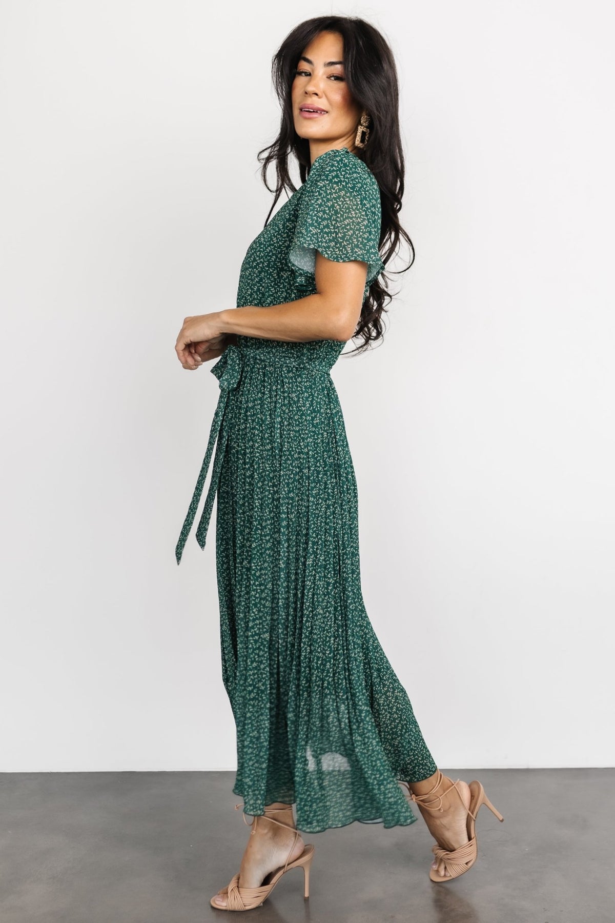 Side angle of the pleated midi dress highlighting gathered waist, removable self-tie, and flowing chiffon skirt.