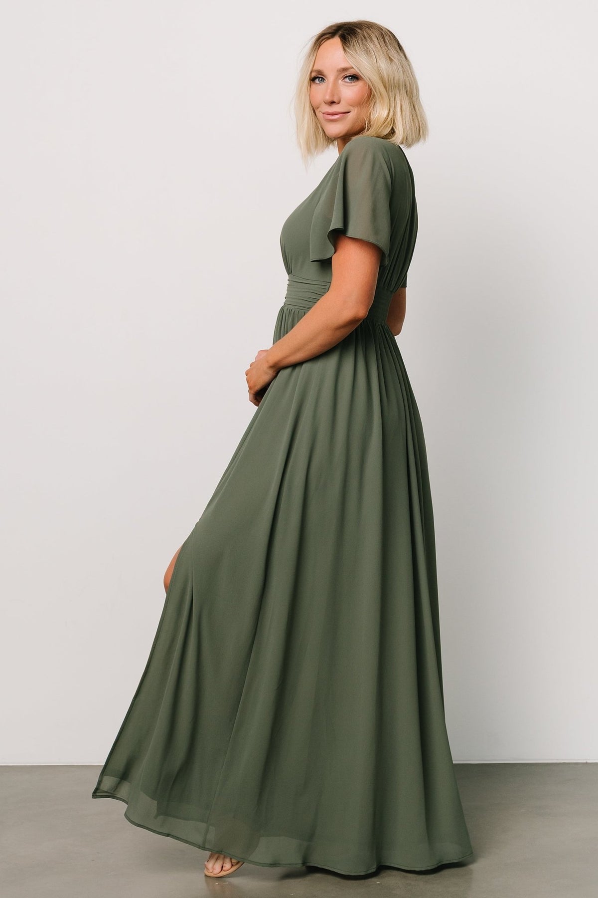Model walking in the Ramona Maxi Dress dark sage, showing movement of the chiffon skirt and elegant occasion-ready styling.