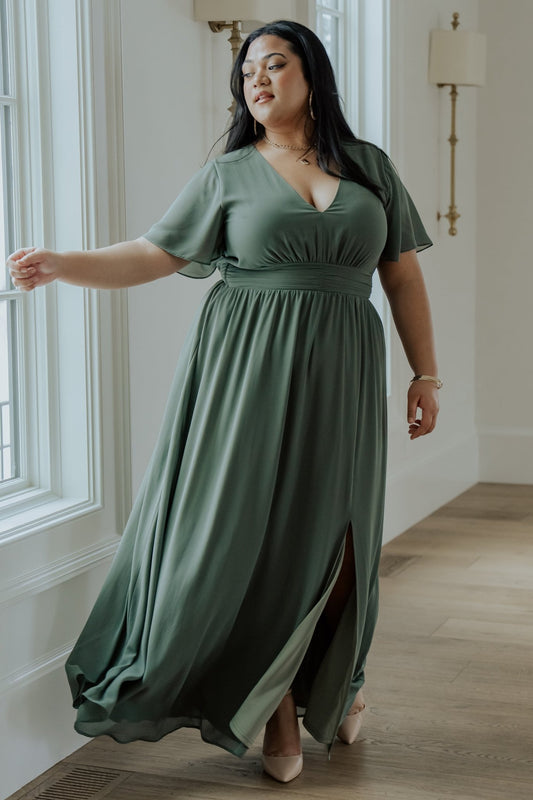 Front view of model wearing Ramona Maxi Dress in dark sage, V-neck, flutter sleeves, smocked back, left leg slit, flowing chiffon drape.