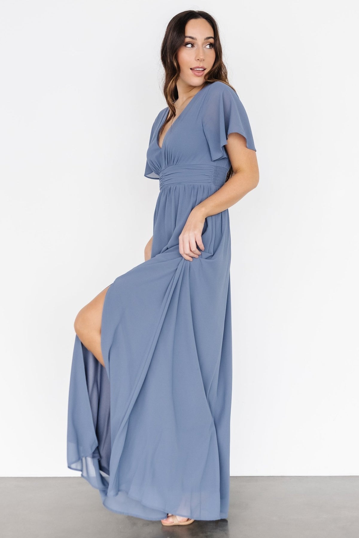 Model posing with hands at waist to highlight smocked detail and empire ruching, emphasizing comfortable shaping.