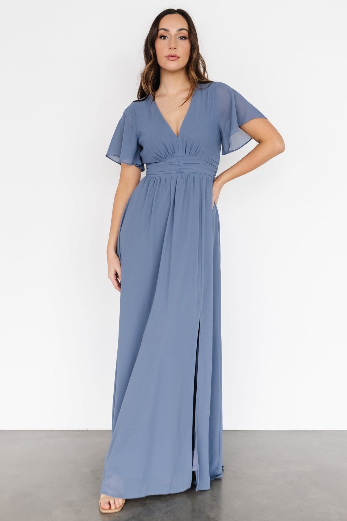 Three-quarter angle showing V-neck bodice, empire waist ruching and full chiffon skirt that flows to the floor with subtle movement.