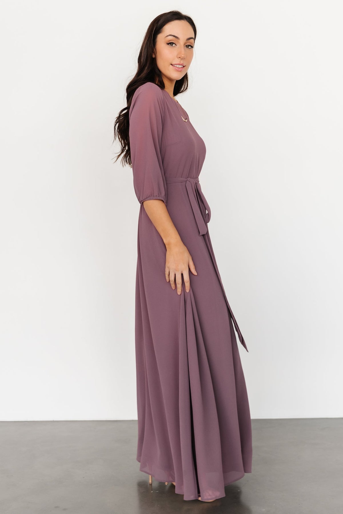 Model wearing Rebecca Maxi Dress vintage plum, elbow sleeves visible, demonstrating fit and length to floor.