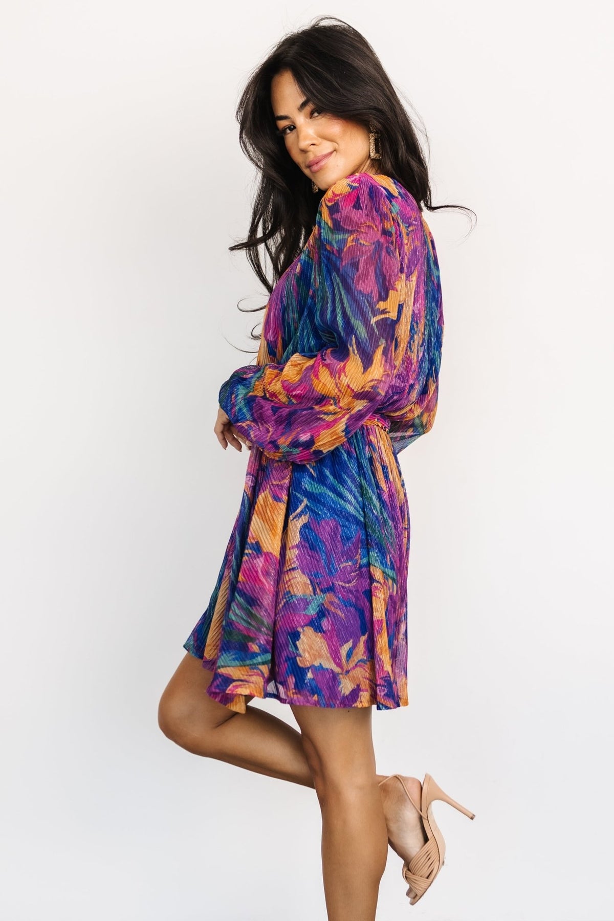 Three-quarter view of the Rev pleated mini dress in blue multi print showing crossover neckline, elastic cuffs, and pleated skirt movement.