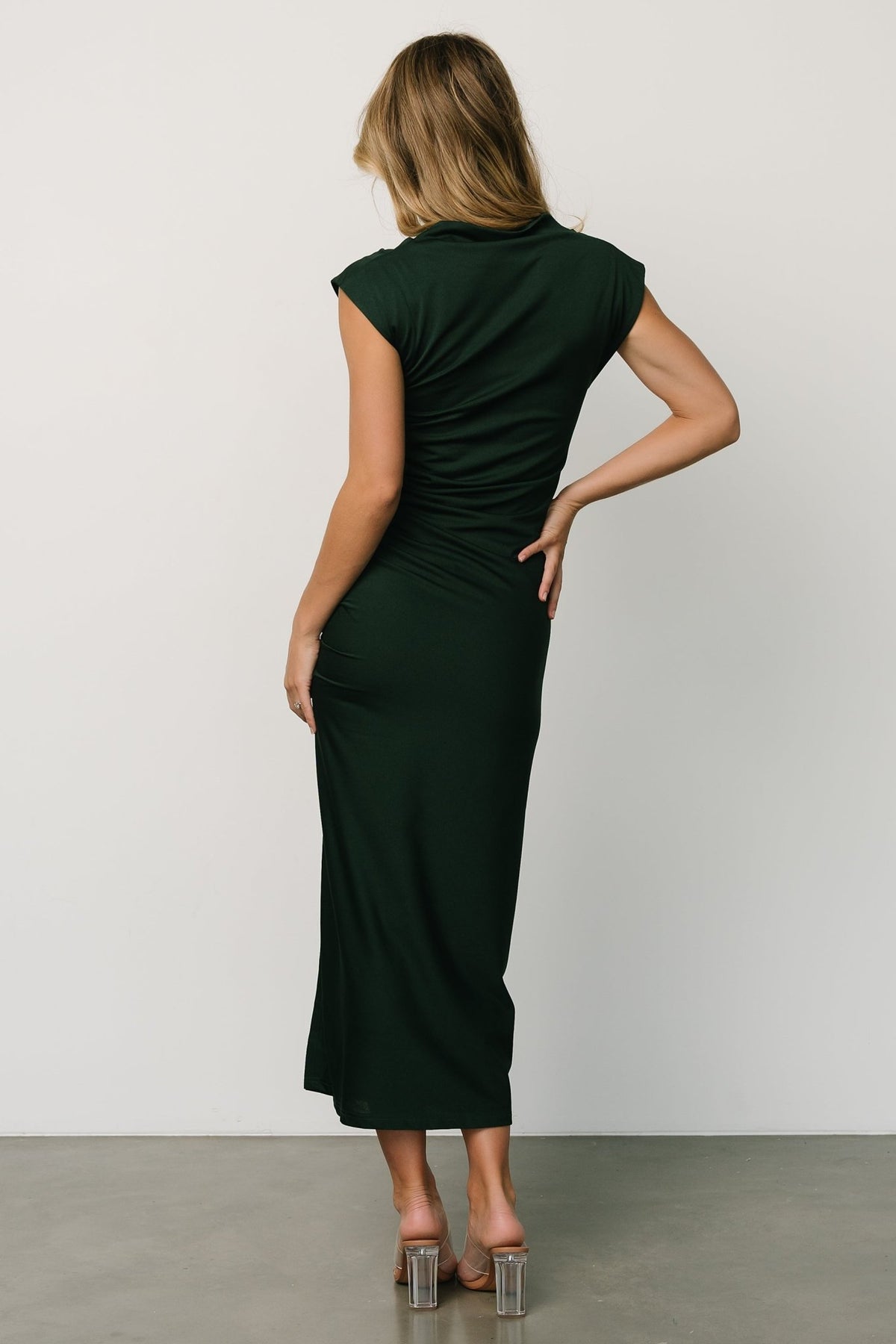 Three-quarter angle of Sasha Ruched Maxi Dress in deep green on model, showing left leg slit, ruched waist and flowing maxi silhouette.