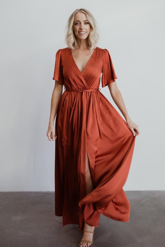 Side profile of the rust satin-like maxi dress showing the silhouette, elastic waist, and how the removable sash shapes the waist.
