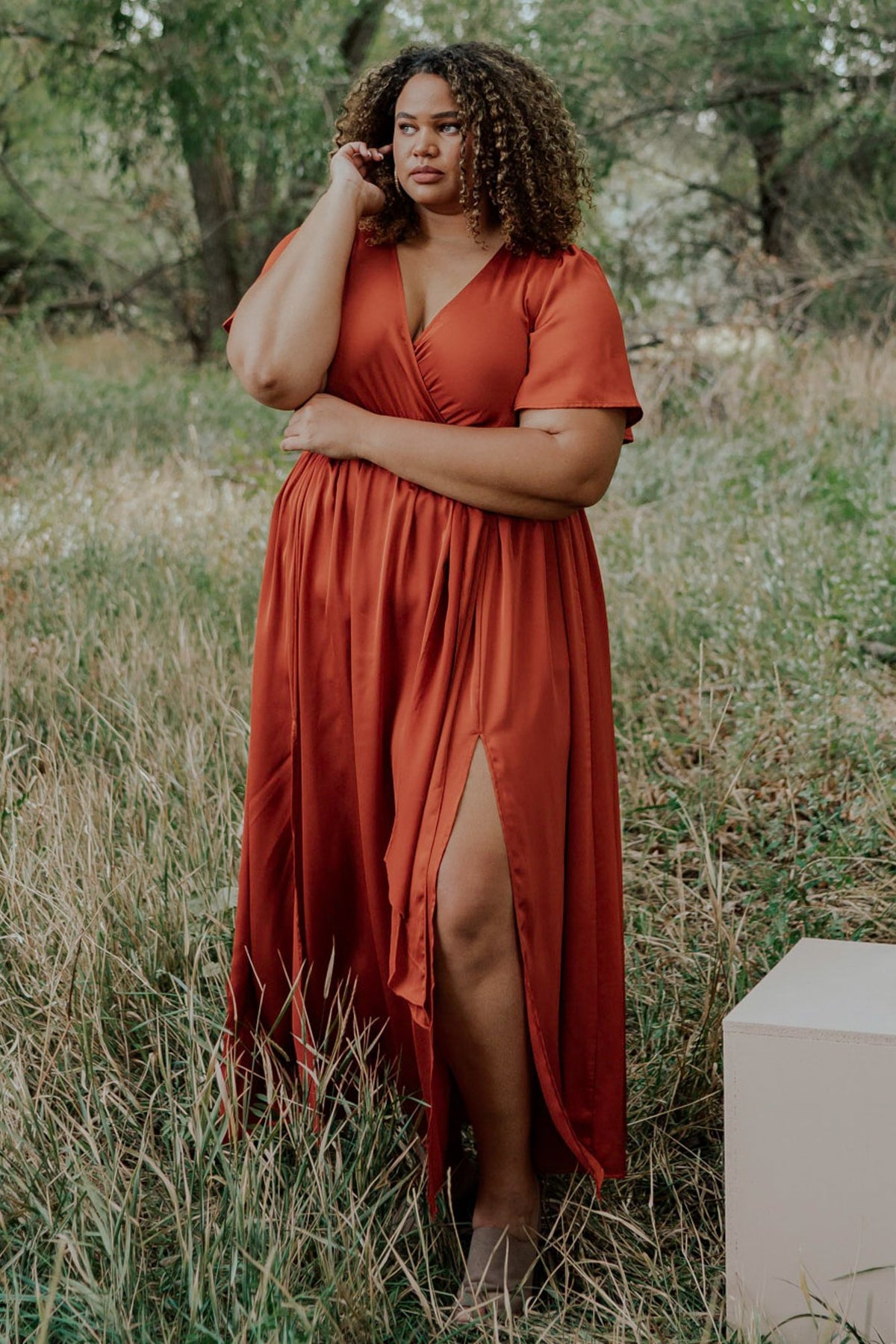 Close-up three-quarter view showing the satin-like textured fabric, crossover surplice neckline and delicate flutter sleeve detail in rust color.