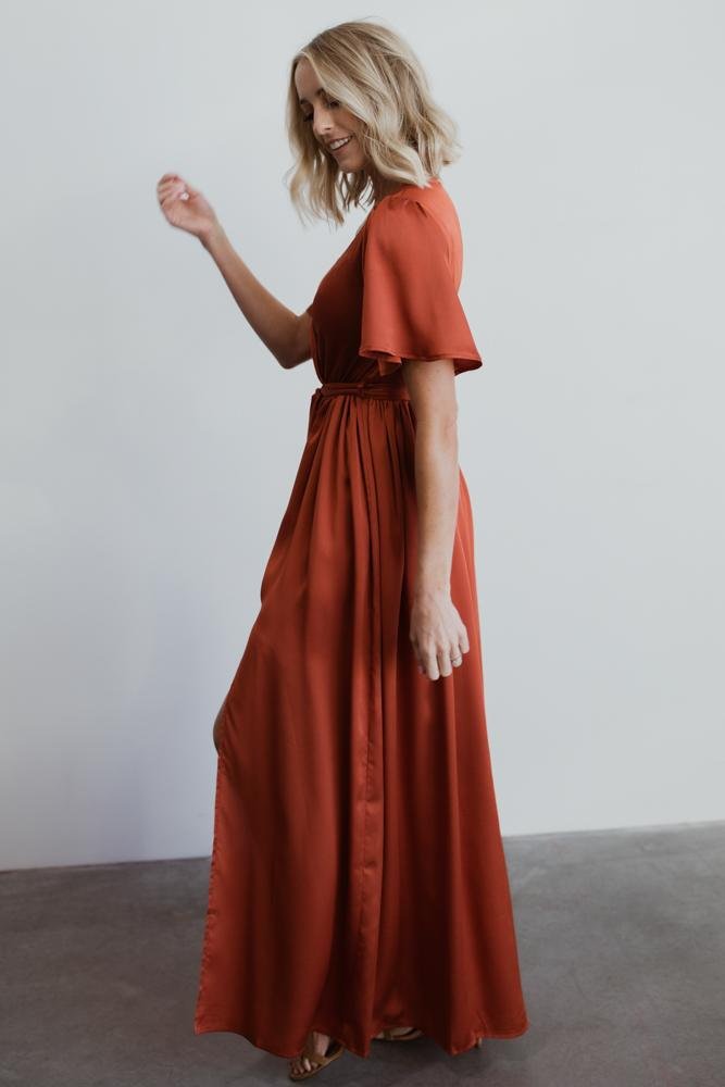 Detail shot of the removable self-tie sash and gathered elastic waist on the rust satin-like maxi dress, showing texture and finish.