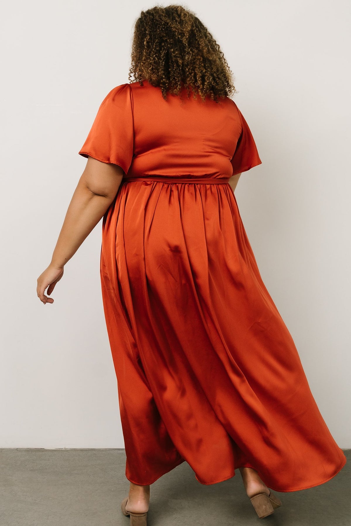 Close-up of fabric sheen and skirt drape on the rust satin maxi, emphasizing the textured finish and lightweight polyester construction.