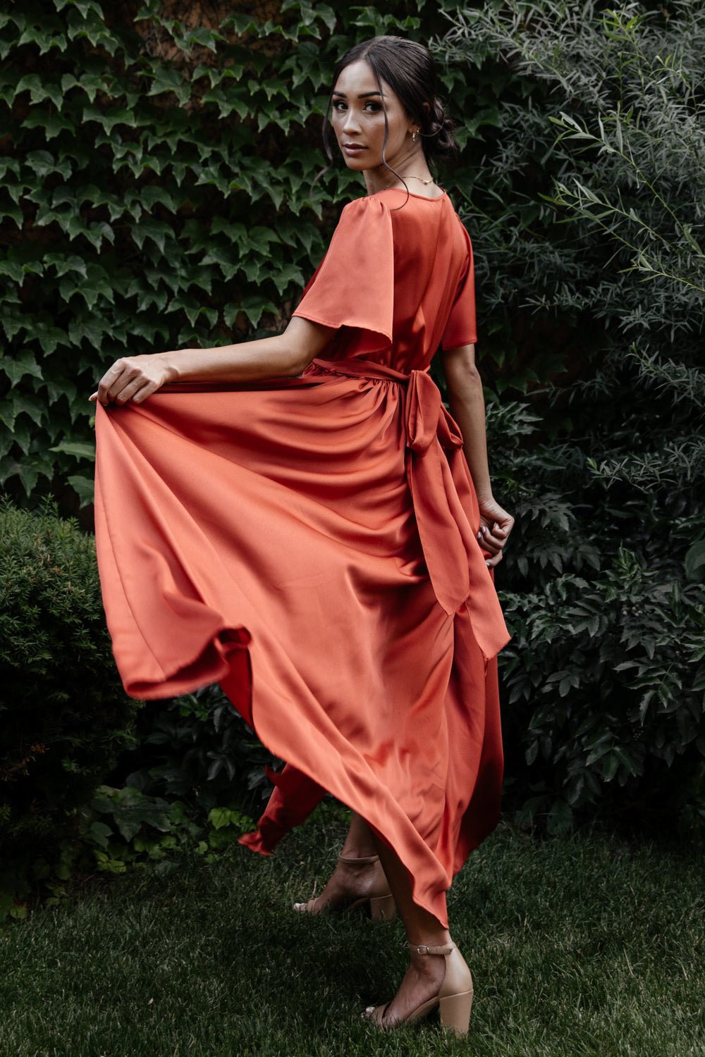 Back and side view of rust maxi dress highlighting the elasticized waistband, flowing skirt silhouette and subtle sheen of the fabric.