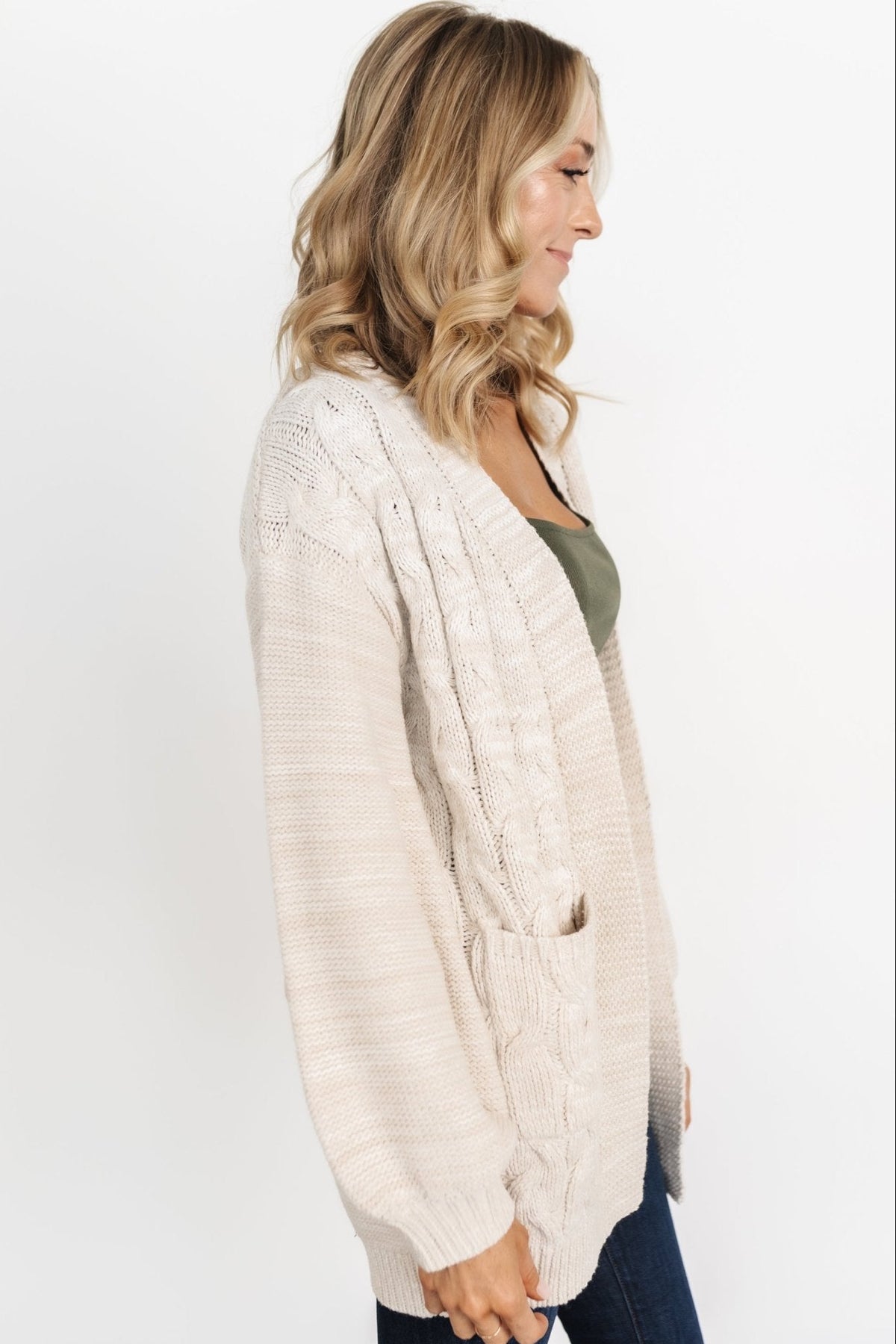Model seated wearing the oatmeal Spencer cardigan layered over a tee, showcasing relaxed drape and front pockets.