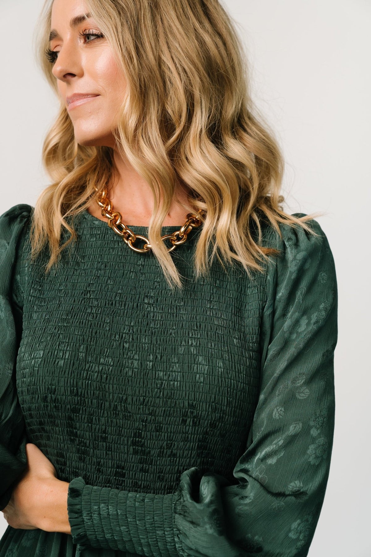 Angled side view of the dark green Stockholm Smocked Dress showing sleeve length, smocked cuffs, and flowing tiered skirt on a model.