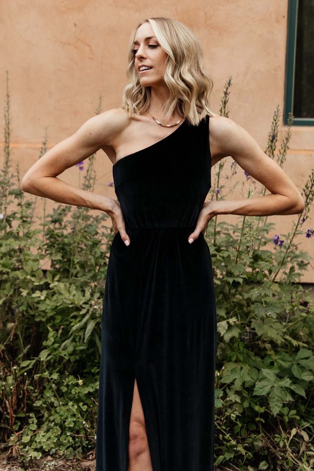 Full-length side view of black velvet maxi dress on model, highlighting the right-side slit and fluid skirt movement.