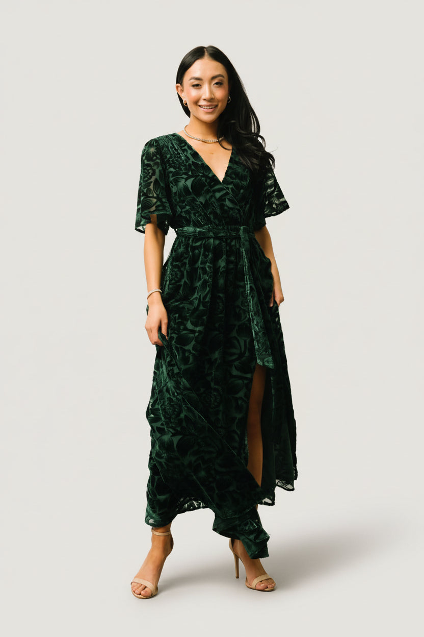 Model wearing the dark green Uma Velvet Maxi Dress full-length, styled with the detachable sash tied at the waist and relaxed short sleeves.